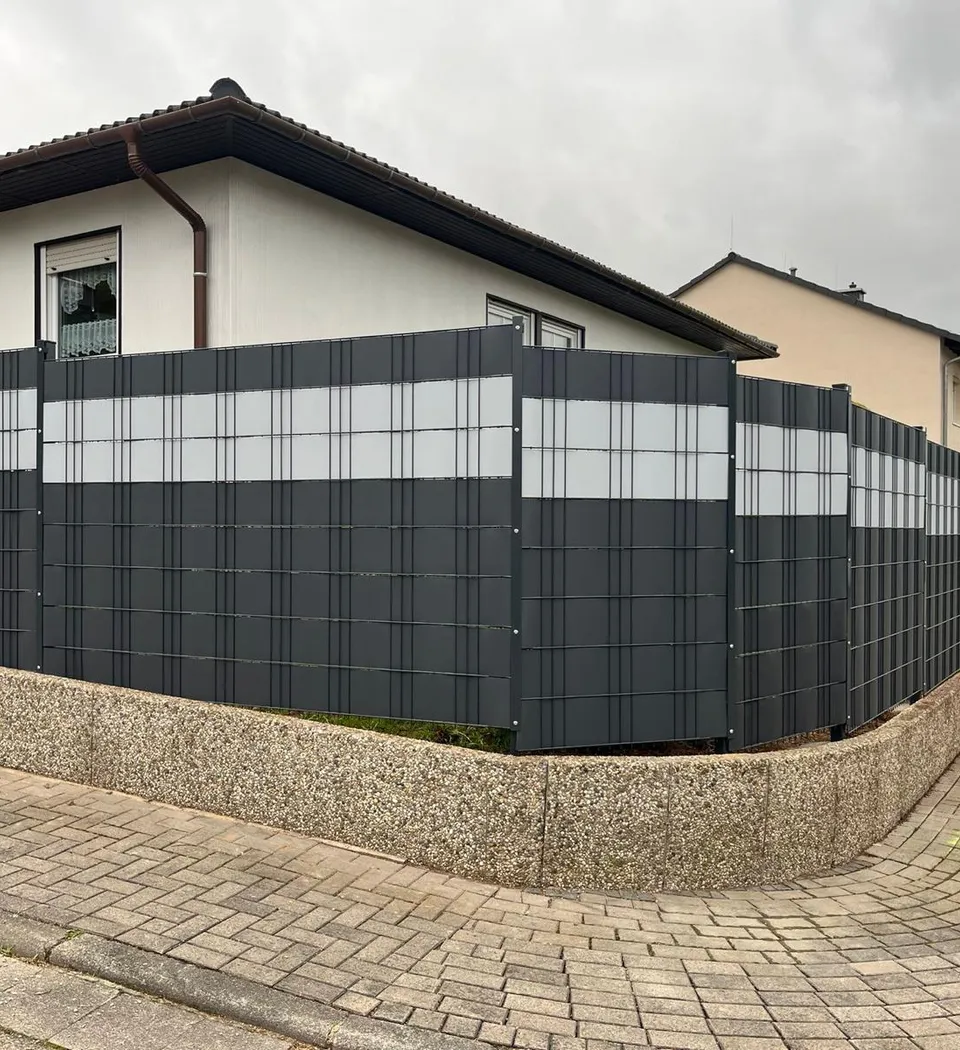 Doppelstabmattenzaun mit Sichtschutzstreifen um ein Eckgrundstück, gesetzt auf eine bestehende Mauer