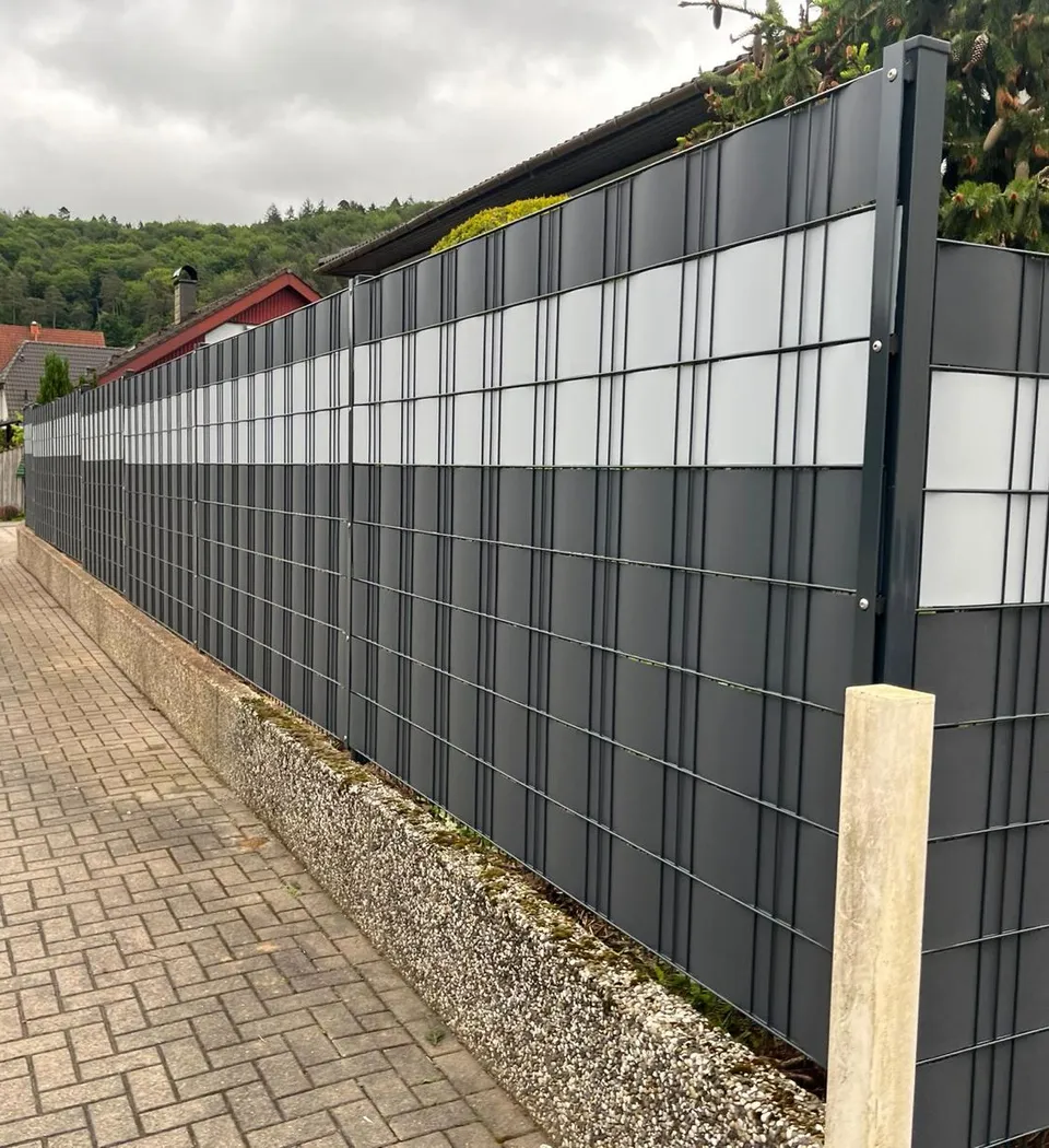 Doppelstabmattenzaun in Anthrazit mit weißen Sichtschutzstreifen auf einer Stützmauer entlang einer Ortsstraße in Waldfischbach-Burgalben