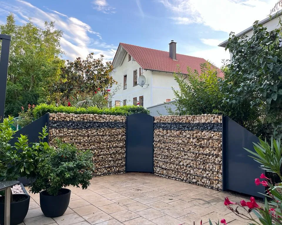 Gabionenwand mit Natursteinfüllung und anthrazitfarbener Gartentür als Abgrenzung einer Terrasse