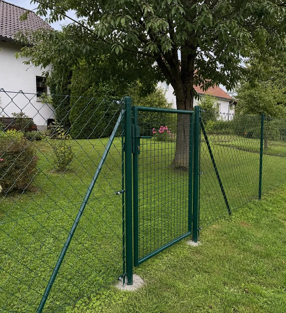 Grün beschichteter Maschendrahtzaun mit Gartentor an einem Wohnhaus