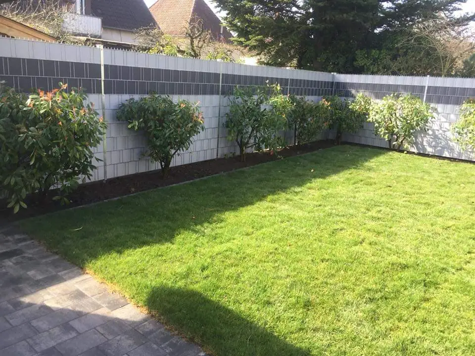 Sichtschutzzaun mit hellen Streifen als Gartenbegrenzung mit frisch gepflanzter Hecke