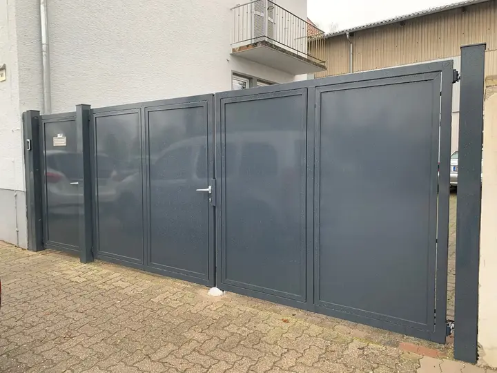 Anthrazitfarbenes zweiflügeliges Stahltor mit geschlossenen Blechfeldern und separatem Eingang links
