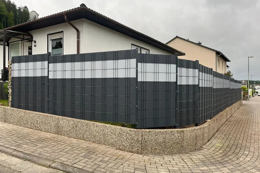 Doppelstabmattenzaun mit Sichtschutzstreifen um ein Eckgrundstück, gesetzt auf eine bestehende Mauer