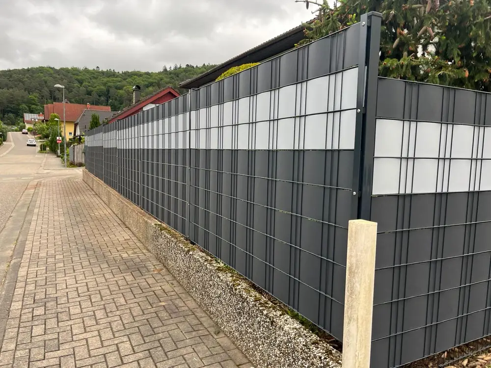 Doppelstabmattenzaun mit eingezogenen Sichtschutzstreifen über eine lange Flucht entlang einer Ortsstraße