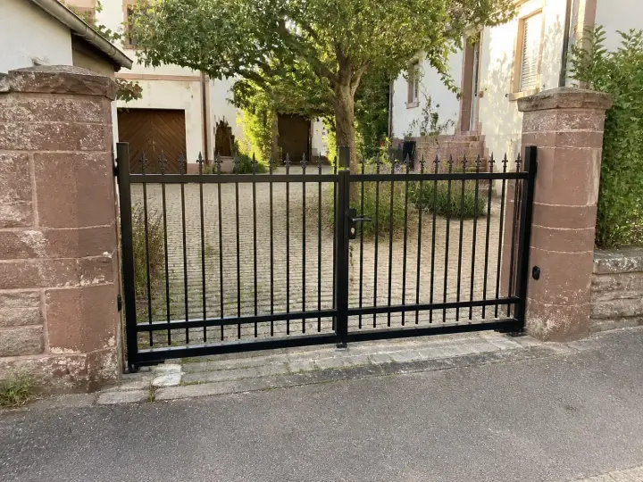Klassisches schmiedeeisernes Einfahrtstor in Schwarz mit Zierspitzen zwischen Sandsteinpfeilern