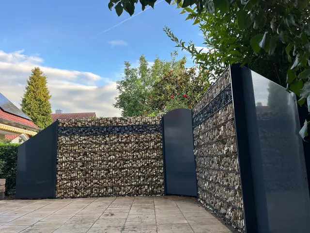Gabionenwand mit Natursteinfüllung und anthrazitfarbenen Sichtschutzelementen an einer Terrasse in Obersülzen