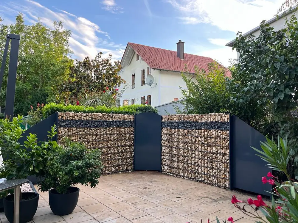 Gabionenwand mit Natursteinfüllung und anthrazitfarbener Gartentür als Abgrenzung einer Terrasse