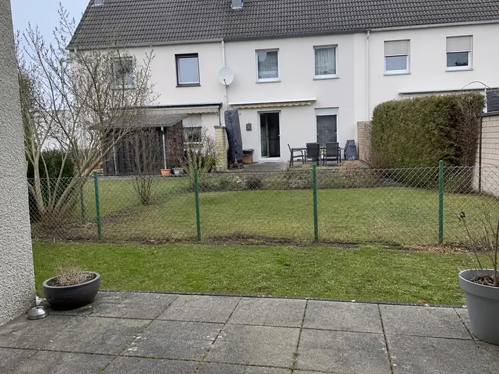 Offene Grundstücksgrenze in einem Reihenhausgarten mit niedrigem Maschendrahtzaun und Terrasse im Vordergrund