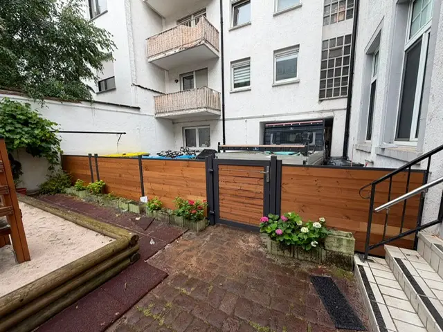 ThermoHolz-Sichtschutz mit anthrazitfarbenen Pfosten und passendem Holztor in einem Innenhof