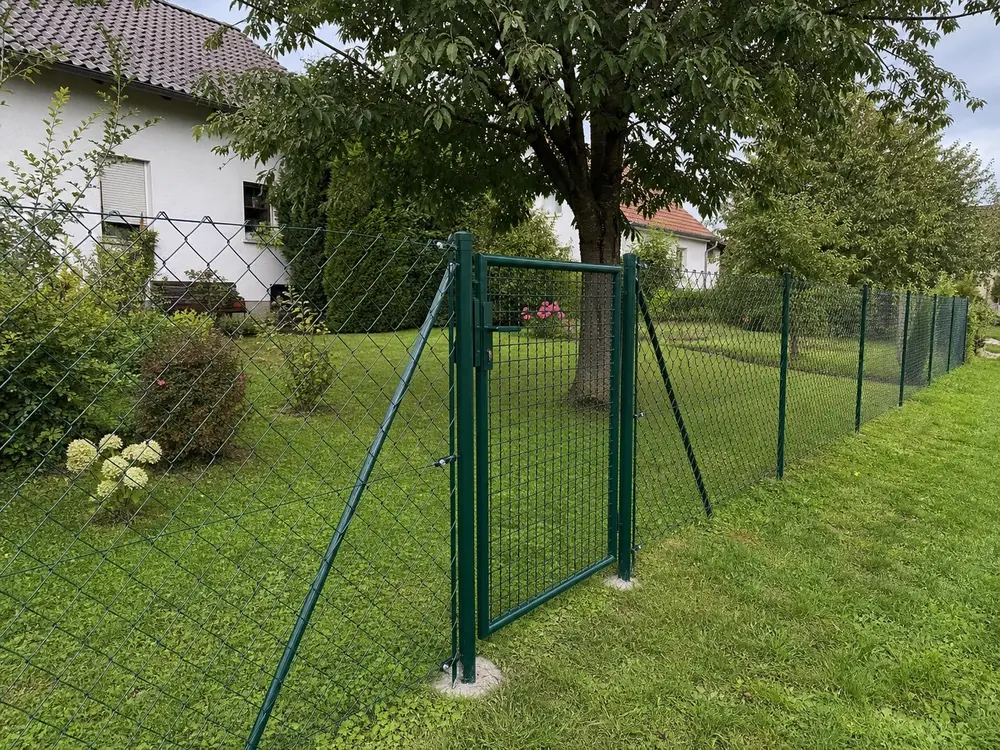 Grün beschichteter Maschendrahtzaun mit Gartentor an einem Wohnhaus