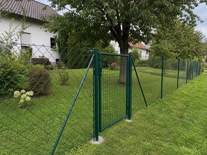Grün beschichteter Maschendrahtzaun mit Gartentor an einem Wohnhaus